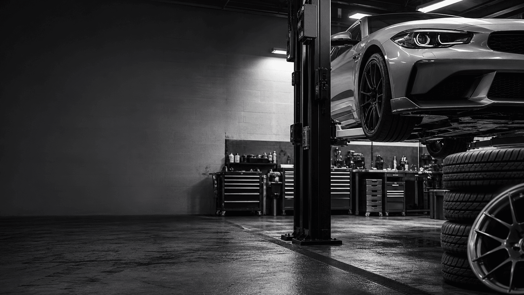 Monochrome auto repair shop bay with a performance car, lift, tools, and tires